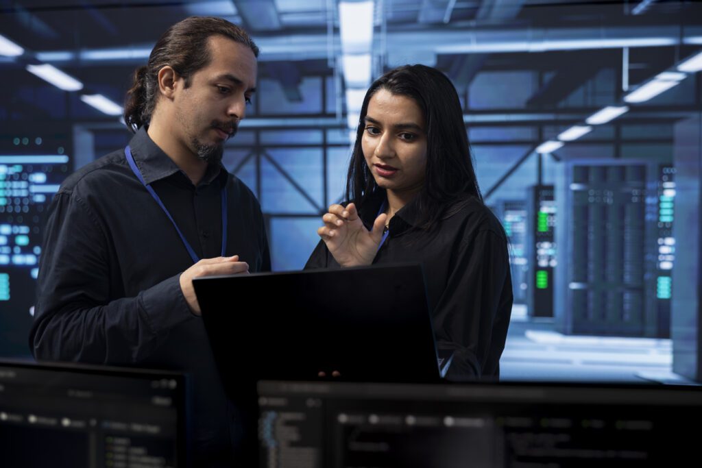 In a server room, two people discuss data protection strategies as they examine crucial information on a laptop.