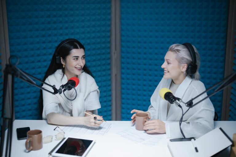 Two women engaged in a lively podcast discussion inside a professional studio setting.