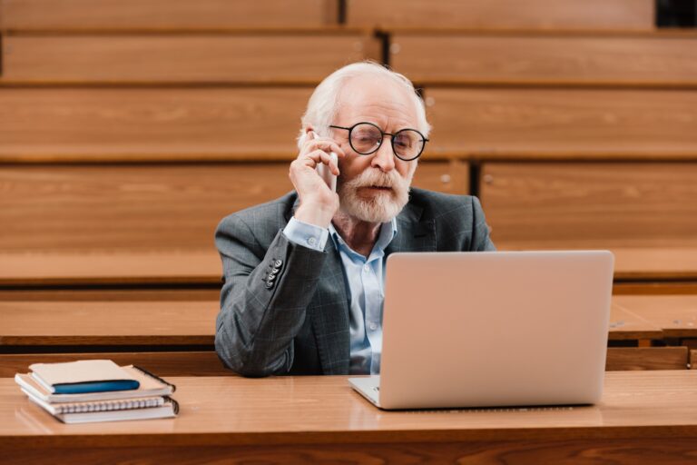 grey hair professor talking by smartphone and looking at laptop