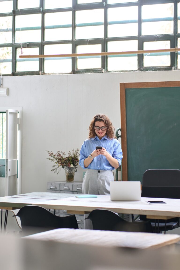Happy young woman using cell phone standing in office at work.