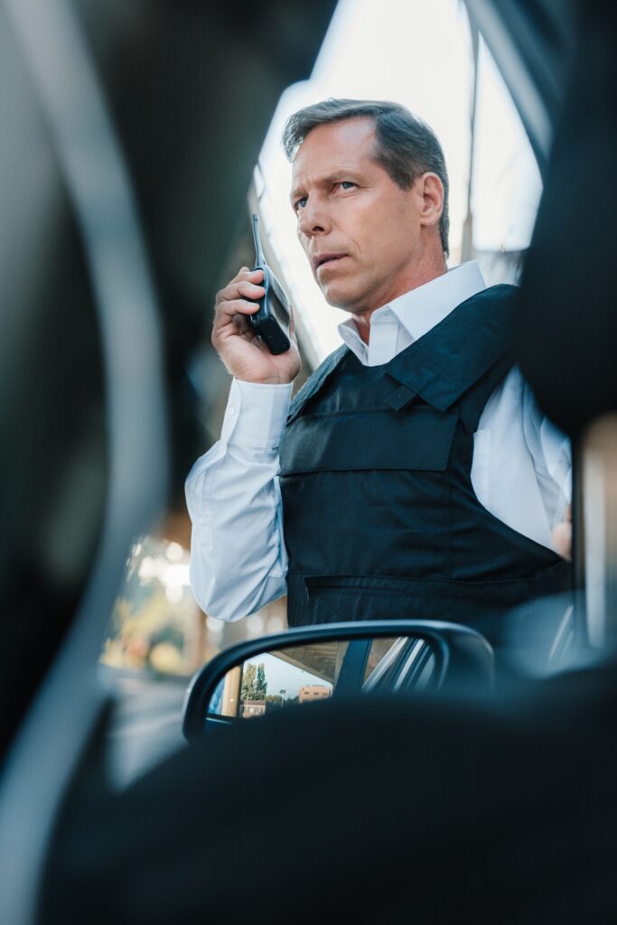low angle view of serious mature male police officer in bulletproof vest talking on radio set near