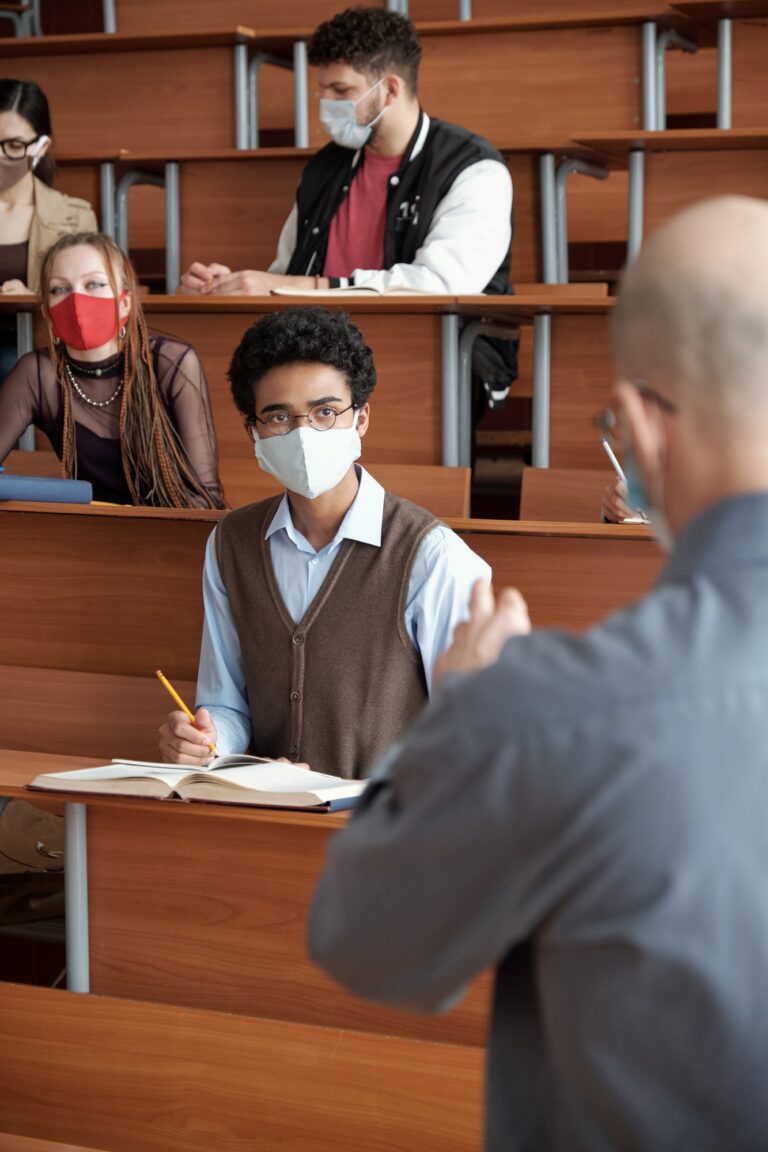 Mixed-race students in mask looking at professor