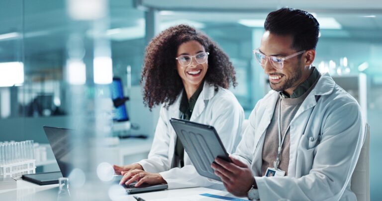 Science, teamwork and laptop with laughing in laboratory for communication, pharmaceutical review o