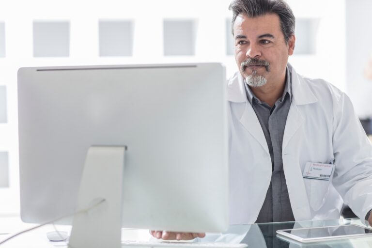 Doctor in a white coat analyzing data on a computer screen.