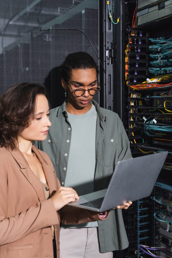 multiethnic technicians working on laptop near server in data center