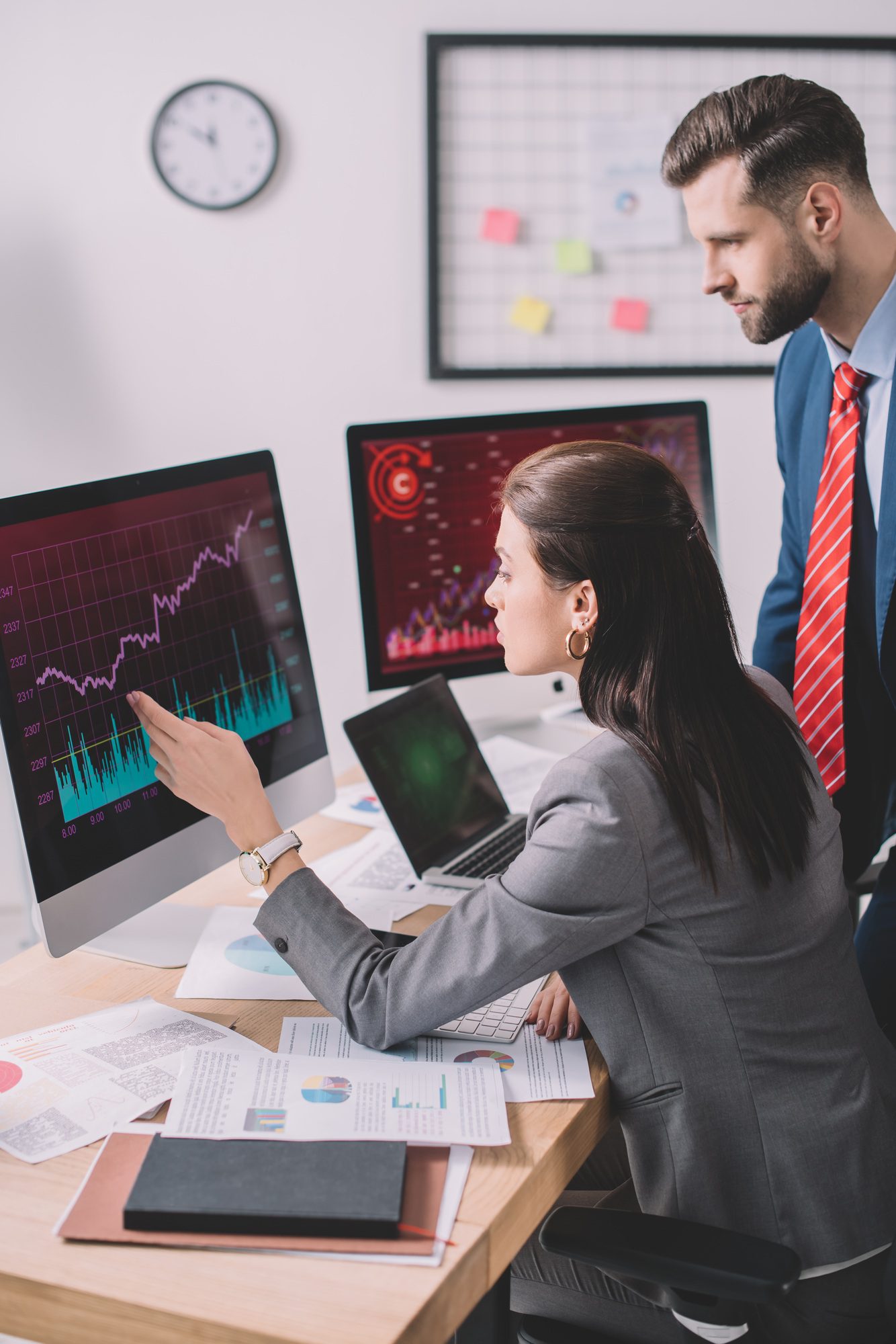 Side view of data analyst pointing with hand at graphs on computer monitor to colleague in office